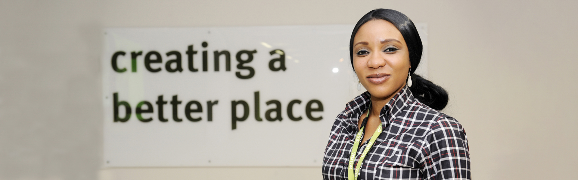 Staff member smiling at the camera with a "creating a better place" sign in view behind them.